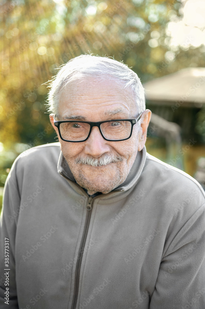 cheerful gray-haired old man looks at the interlocutor and smiles. The old man can't see very well without his glasses. Portrait of a cheerful old man with glasses close-up