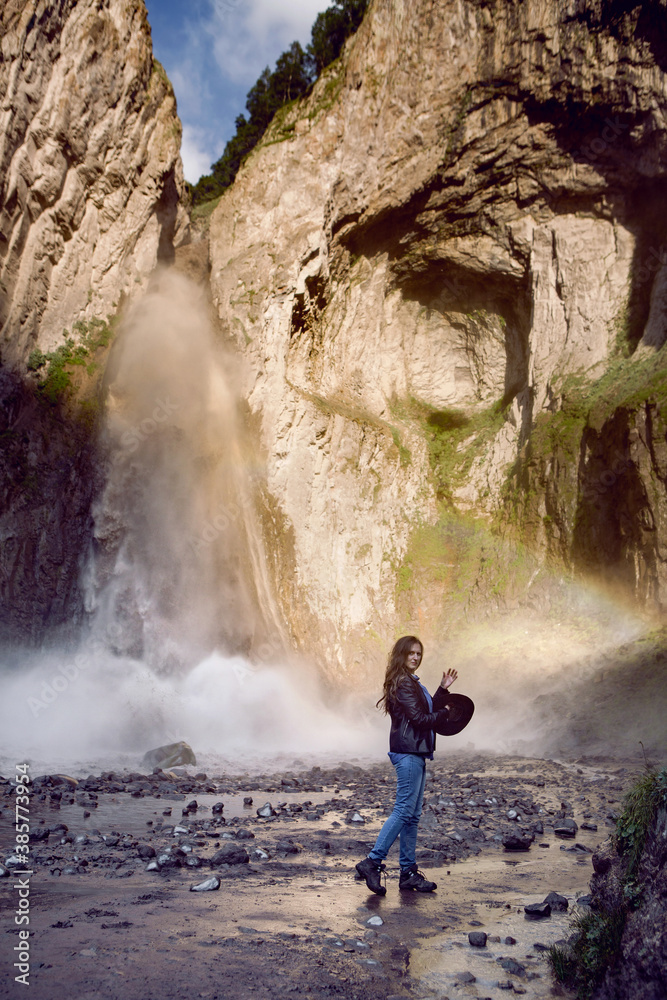 a girl in jeans and boots stands next to a waterfall in the summer