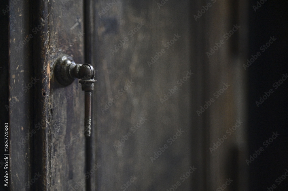 Close-up of the black iron door handle on the wooden cabinet door against a blurred background. Close-up of the black iron door handle on the wooden cabinet door against a blurred background.