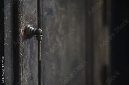 Close-up of the black iron door handle on the wooden cabinet door against a blurred background. © Moment Capsule
