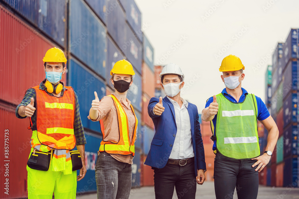Factory worker and engineer team wearing protection face mask against coronavirus ( COVID-19 ) with giving thumbs up at cargo containers Factory worker and engineer team wearing protection face mask against coronavirus ( COVID-19 ) with giving thumbs up at cargo containers
