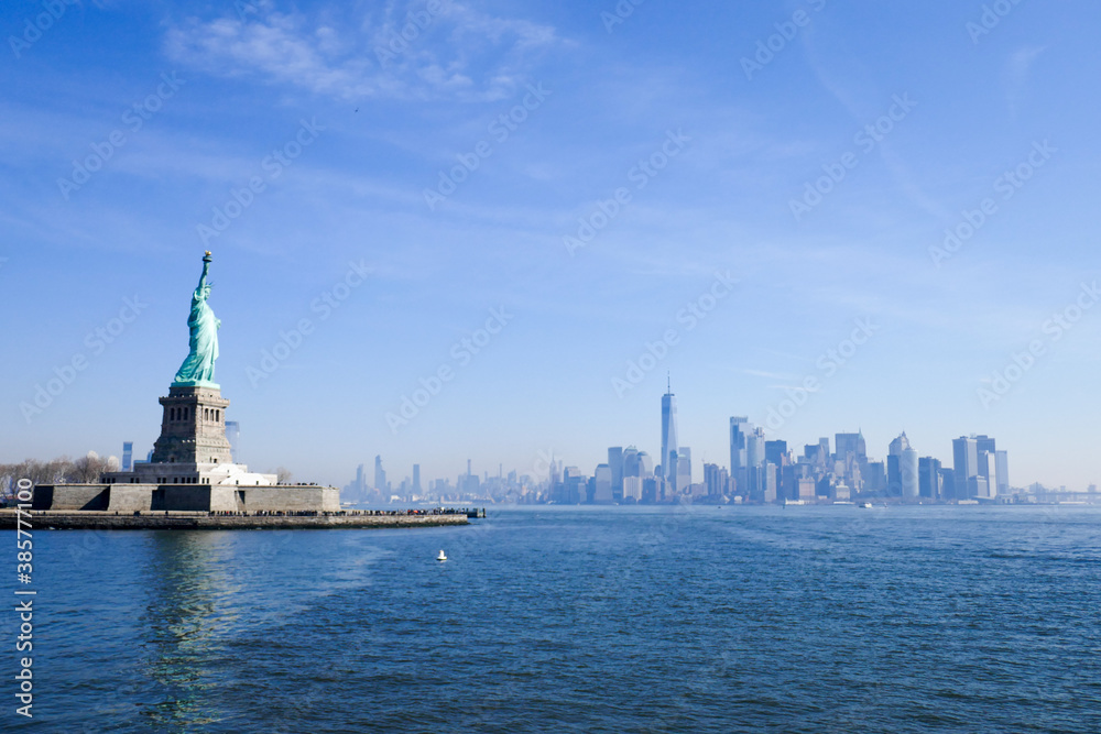 Statue of Liberty in NY Harbor on bright sunny day with blue sky and Manhattan in the distance Statue of Liberty in NY Harbor on bright sunny day with blue sky and Manhattan in the distance