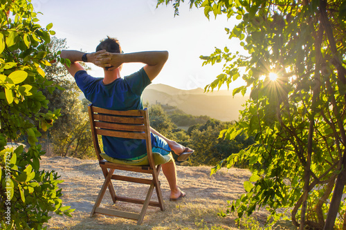 idyllic and rural scene. A man chilling and resting after hiking sitting on a wooden chair and looking at the sunset next to his house in the mountains. Congost De Mont Rebei, Lleida, Spain
