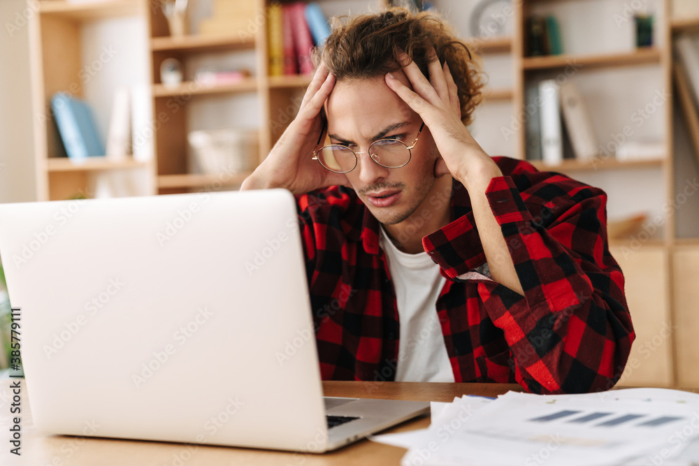 Handsome brooding guy working with laptop while sitting at office Handsome brooding guy working with laptop while sitting at office