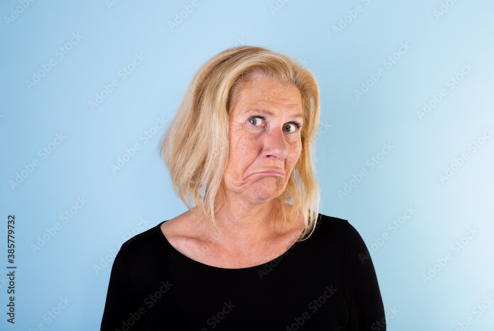 Studio portrait of 60+ woman with blonde page making funny face on light blue background. Studio portrait of 60+ woman with blonde page making funny face on light blue background.
