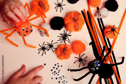 Child makes Halloween decoration and plays with handmade fluffy spiders, bright orange knitted pumpkins, pom poms, pipe cleaners, artificial spiders and skulls . Children craft. Halloween decoration. photo