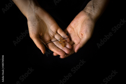 Female hands holding a brown wooden crucifix on a black blur background.The concept of religion Christianity or Catholicism.