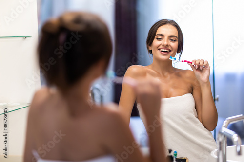 Portrait of beautiful young woman brushing teeth in bathroom