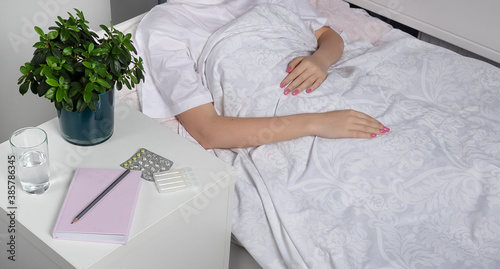 bedside table with medicines and water. The papacy is self-isolating at home.Girl with cold at home under the covers