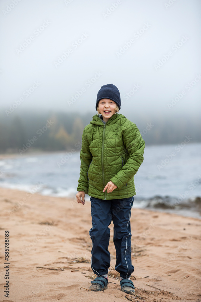 portrait of a girl in a jacket on the shore. Child on the beach by the cold sea.