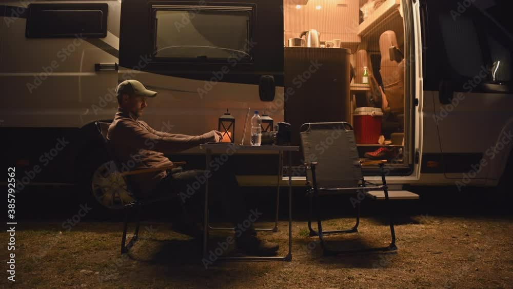 Caucasian Modern Couple Staying Overnight in the RV Park with Their Camper Van. Men Working Online, Woman Preparing Hot Tea Inside the Motorhome.