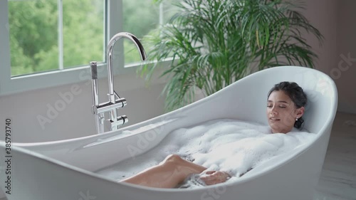 Relaxed woman in bath in slow motion. Sexy girl taking bathtub with bubbles and foam in slow motion. Top view of pretty lady enjoying in luxury bathroom