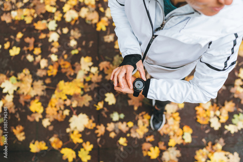 Caucasian female runner starting activity on smartwatch. Woman monitoring a heart rate on her watch outdoors. Top view with yellow leaves background. Running people and modern devices concept image.