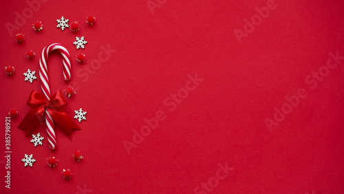 Christmas lollipop with red bow, white snowflakes and red balls on red background, copy space, top view, flat lay.Christmas and New Year decor concept © Komchatnykh Tetiana
