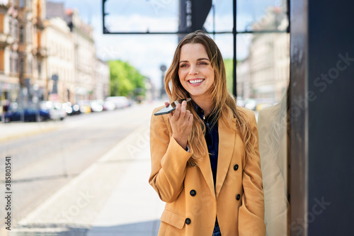 Happy beautiful woman using speaker while talking through smart phone at tram station photo