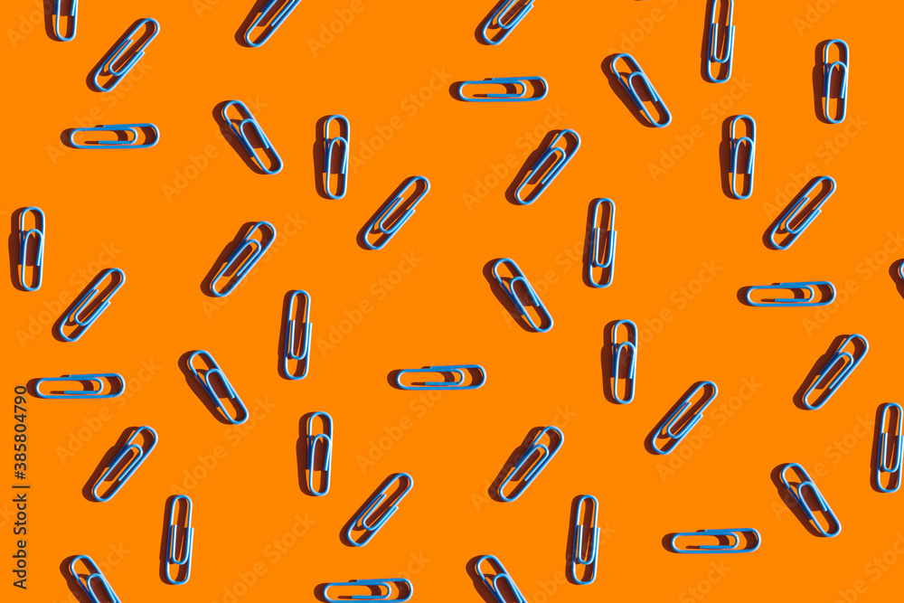 blue paper clips on a bright orange background. School supplies top view. Colorful background blue paper clips on a bright orange background. School supplies top view. Colorful background