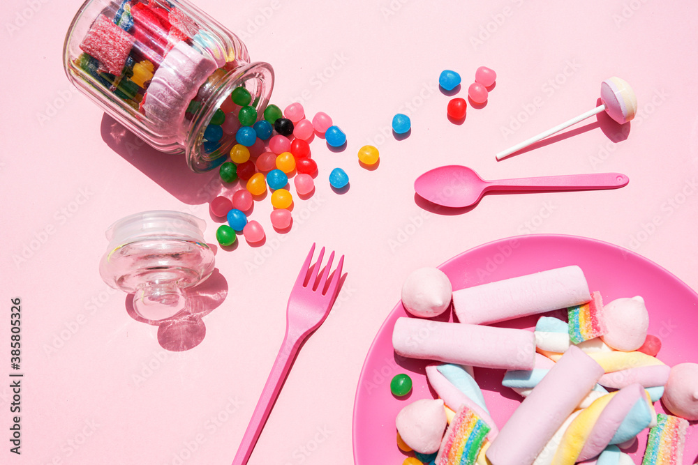 Studio shot of plastic plate filled with various sweets and candies spilling out from toppled jar Studio shot of plastic plate filled with various sweets and candies spilling out from toppled jar