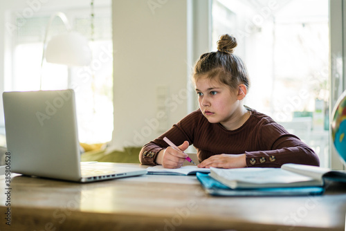 Girl writing in book while studying through laptop at home