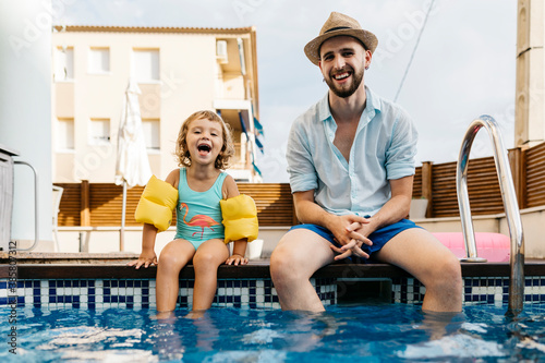 Laughing girl with her uncle sitting on poolside