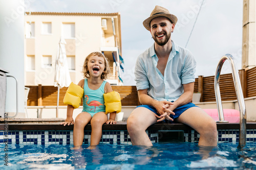 Laughing girl with her uncle sitting on poolside photo