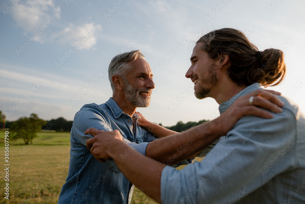 Happy father and adult son facing each other on a meadow in the countryside Happy father and adult son facing each other on a meadow in the countryside