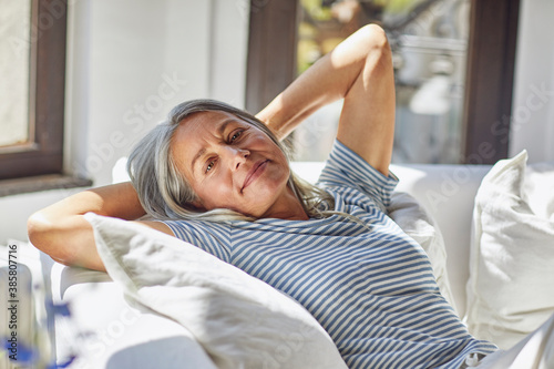 Smiling woman relaxing with hands behind hand on sofa in living room
