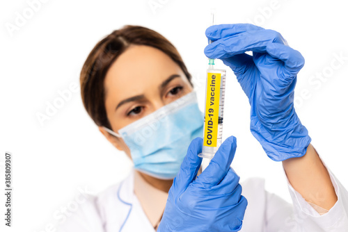 Selective focus of doctor in latex gloves holding syringe with covid-19 vaccine lettering isolated on white