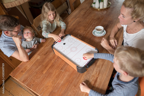 Kids playing air hockey at dining table with parents during weekend photo