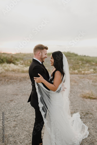 Smiling bride and groom looking at each other in field against sky photo