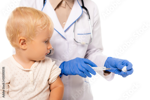 Selective focus of toddler looking at doctor with cotton and syringe isolated on white