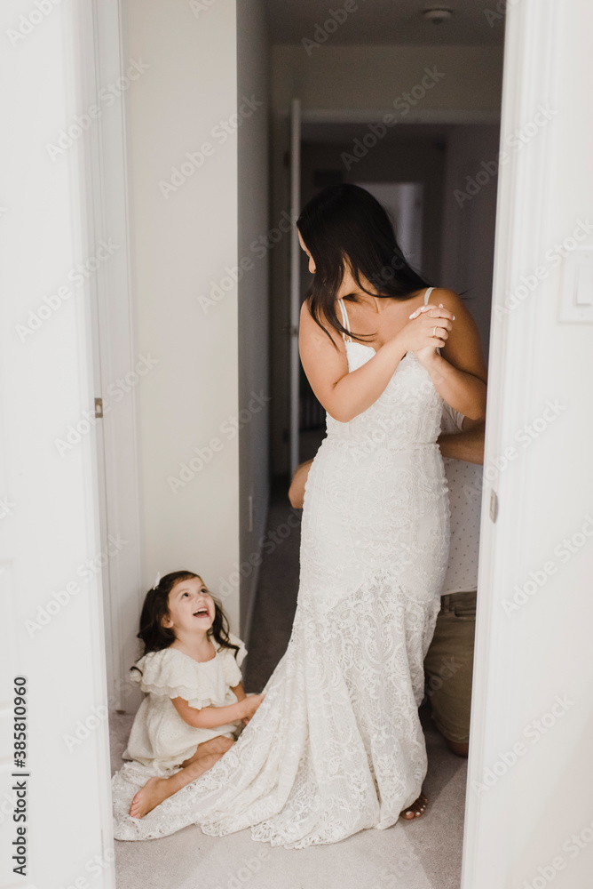 Smiling daughter looking at mother getting dressed for wedding