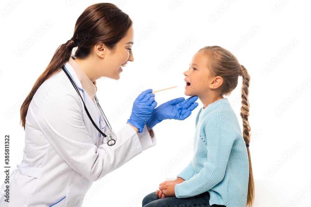 Smiling pediatrist holding stick near child with open mouth isolated on white Smiling pediatrist holding stick near child with open mouth isolated on white
