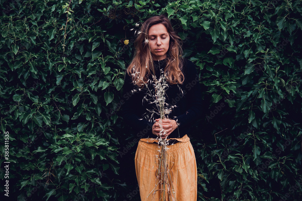 Woman with closed eyes holding dry flowers while standing in park during autumn Woman with closed eyes holding dry flowers while standing in park during autumn