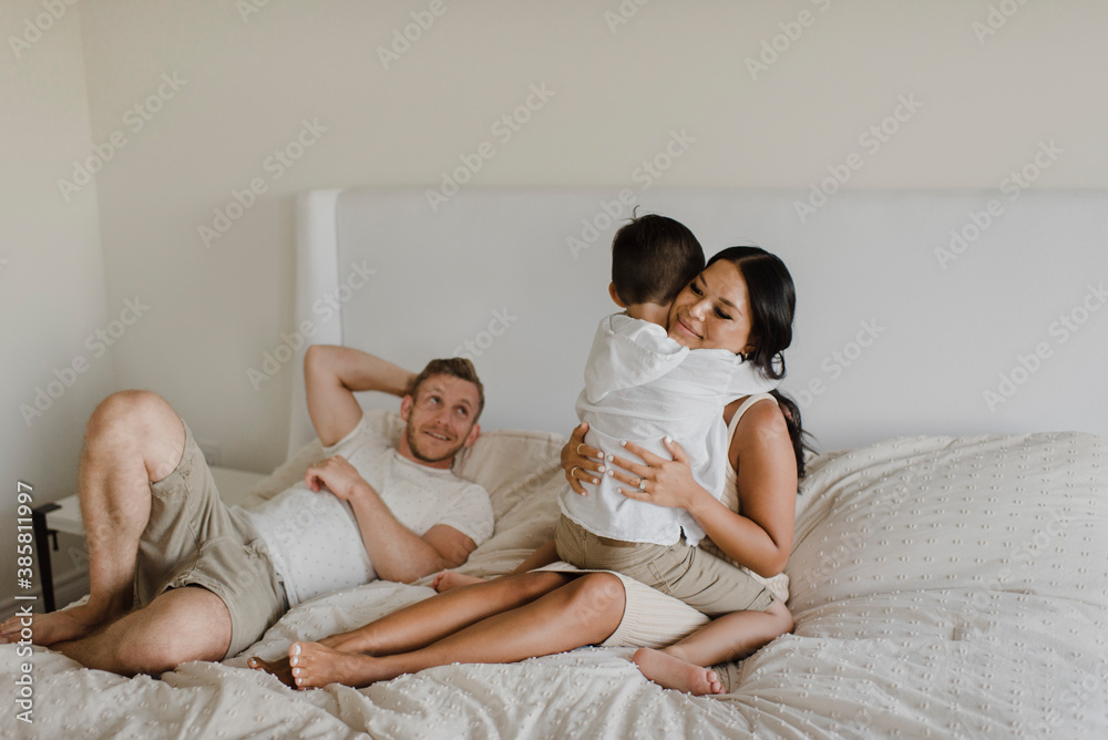 Son embracing mother while father lying on bed in bedroom Son embracing mother while father lying on bed in bedroom