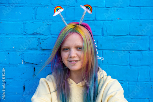 Young woman with dyed hair and rainbow alice band in front of blue wall photo