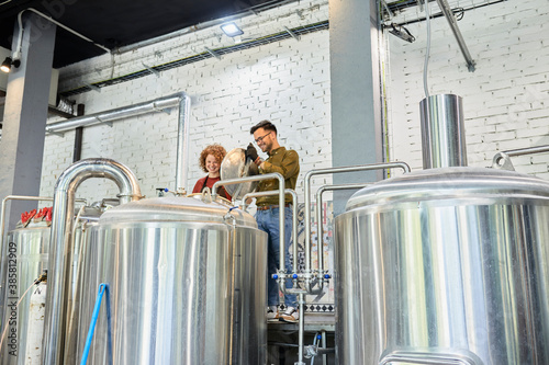 Man and woman working in craft brewery looking into tank photo