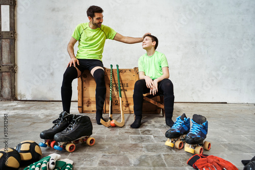 Father sharing light moment with while sitting on wooden box by sports equipment against wall at court photo