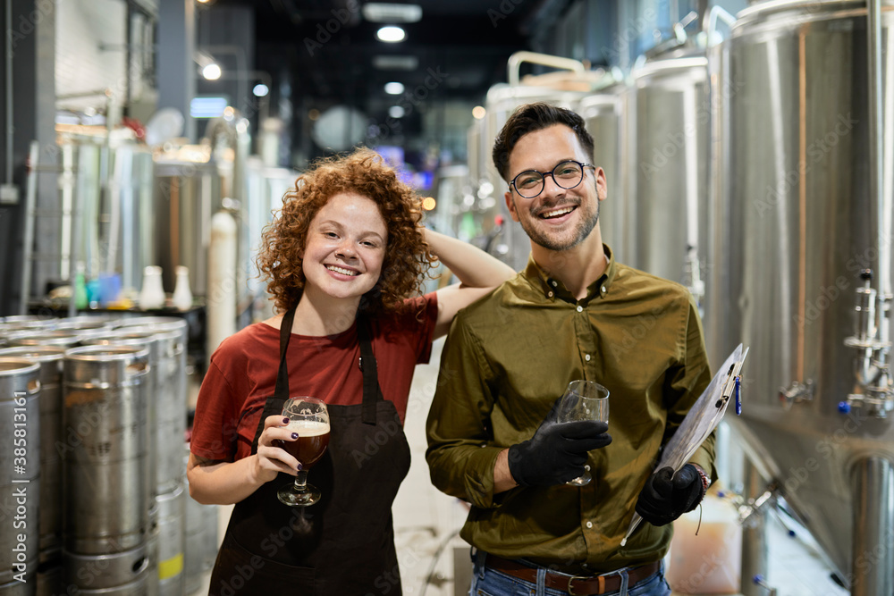 Portrait of happy man and woman holding clipboard and beer glass in craft brewery Portrait of happy man and woman holding clipboard and beer glass in craft brewery