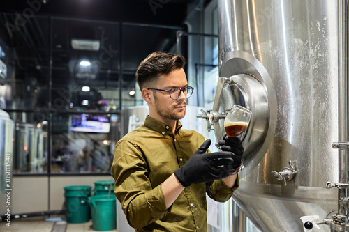 Man working in craft brewery checking quality of a beer photo