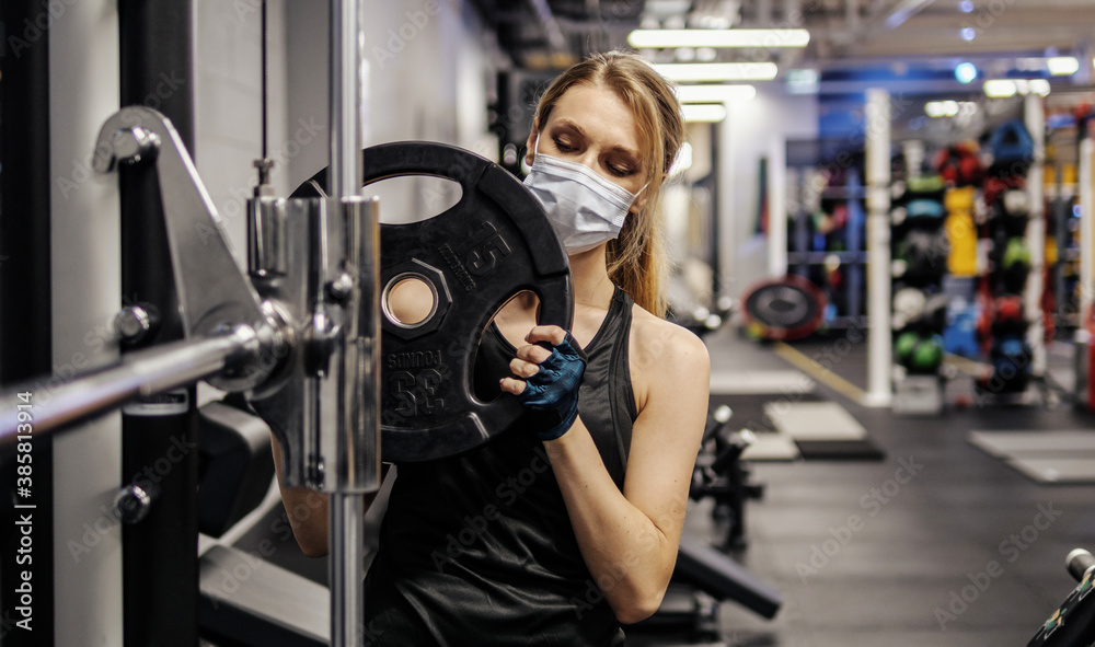 Fototapeta premium Pandemic gym - woman working out with protective face mask during coronavirus outbreak