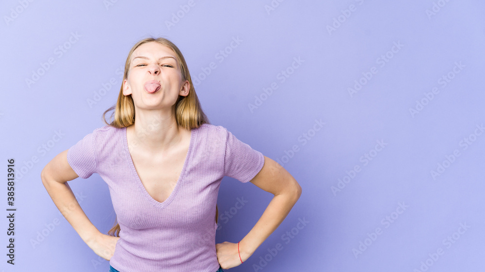Young blonde woman isolated on purple background funny and friendly sticking out tongue.