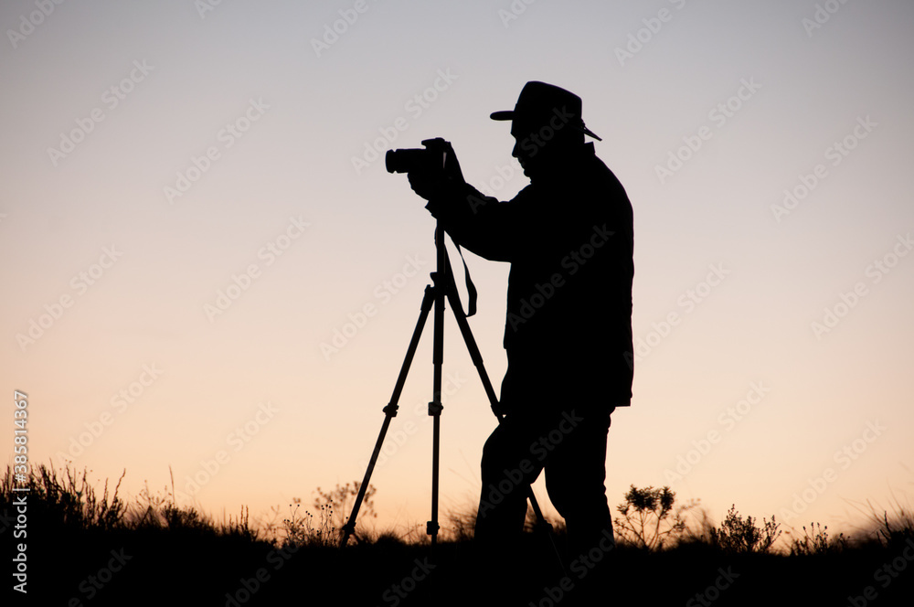 Silhueta de fotógrafo com chapéu e tripé ao pôr-do-sol