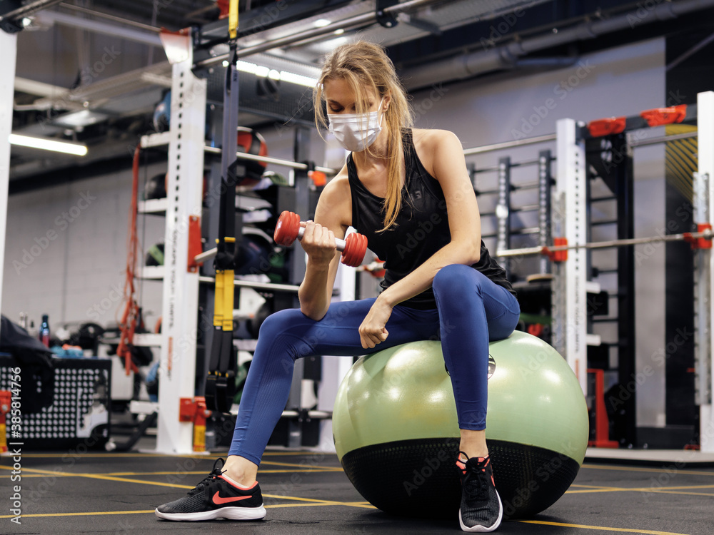 Fototapeta premium Pandemic gym - woman working out with protective face mask during coronavirus outbreak
