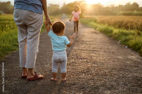 Φωτογραφία mother help her baby to walk her first step on country road