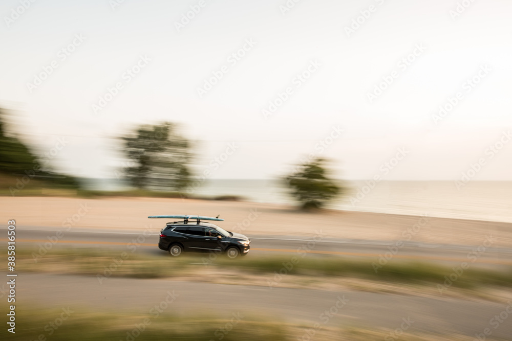 Blurred motion of car with standup paddleboard on top along Lake Michigan Blurred motion of car with standup paddleboard on top along Lake Michigan