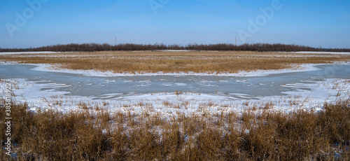 winter frozen river among a dry grass prairie