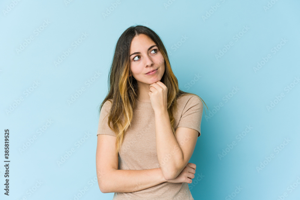 Young caucasian woman isolated on blue background relaxed thinking about something looking at a copy space. Young caucasian woman isolated on blue background relaxed thinking about something looking at a copy space.