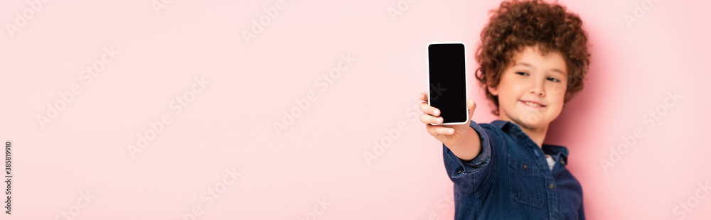 selective focus of curly boy in denim shirt holding smartphone with blank screen on pink, panoramic shot selective focus of curly boy in denim shirt holding smartphone with blank screen on pink, panoramic shot