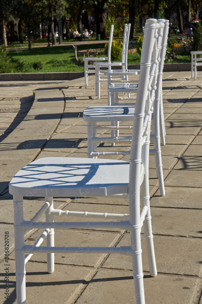 Large group of empty white chairs arranged for social distance, ready to sit visitors to outdoor business conference. COVID-19 health and safety measures during pandemic require spacing between people Large group of empty white chairs arranged for social distance, ready to sit visitors to outdoor business conference. COVID-19 health and safety measures during pandemic require spacing between people