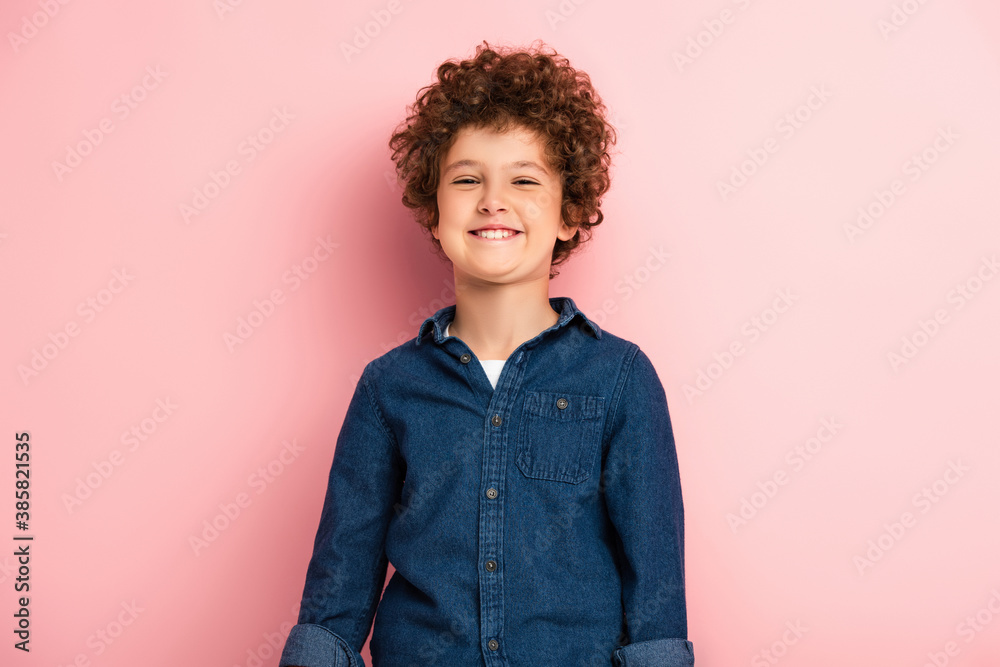 pleased and curly boy in denim shirt smiling on pink pleased and curly boy in denim shirt smiling on pink